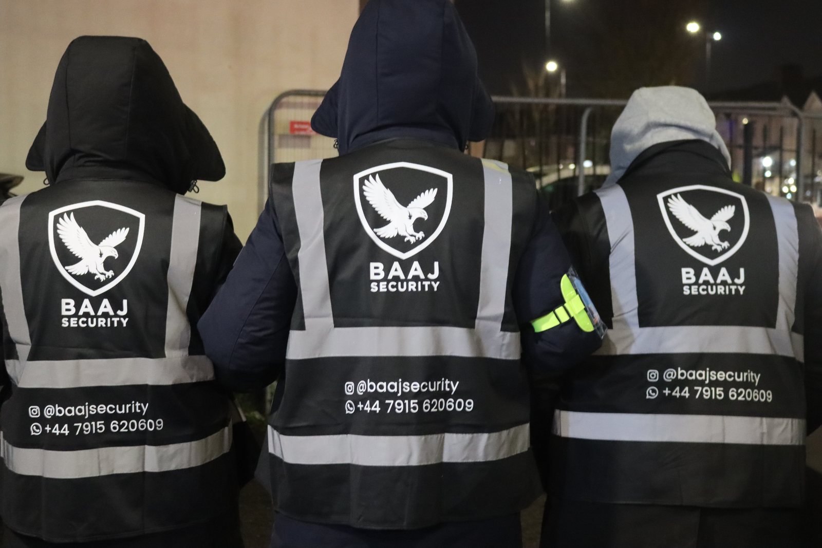 Three SIA-licensed Baaj Security operatives on duty at night in branded Baaj Security hi-vis, 2026